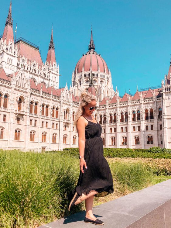 Dívka v černých šatech stojící před budovou Maďarského parlamentu, jedno z míst v Budapešť itinerář