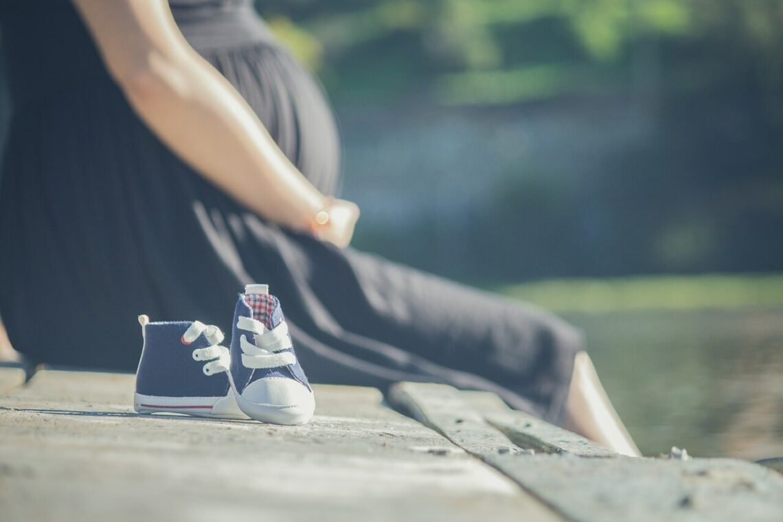 Těhotná žena sedící na lavičce, záběr na těhotenské břicho a před ní dětské botičky - fotka k článku létání v těhotenství