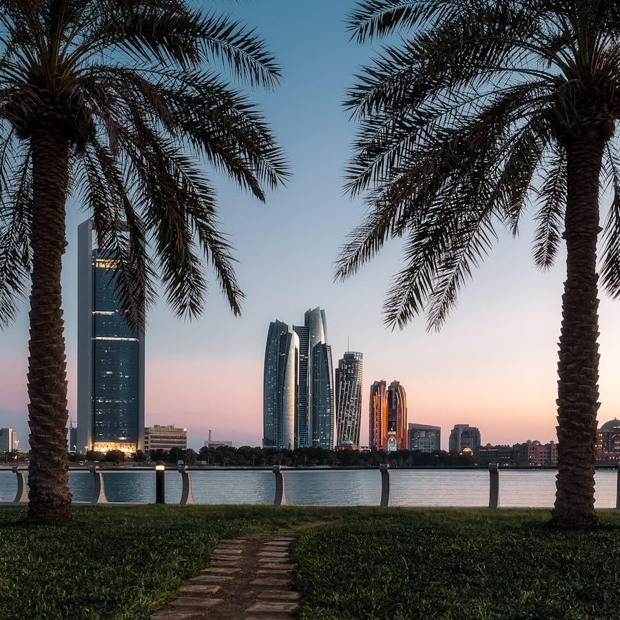 Panoramatický výhled na mrakodrapy Abu Dhabi (včetně Etihad Towers) přes palmy na nábřeží Corniche při západu slunce. Skvělý tip, co vidět v Abu Dhabi.