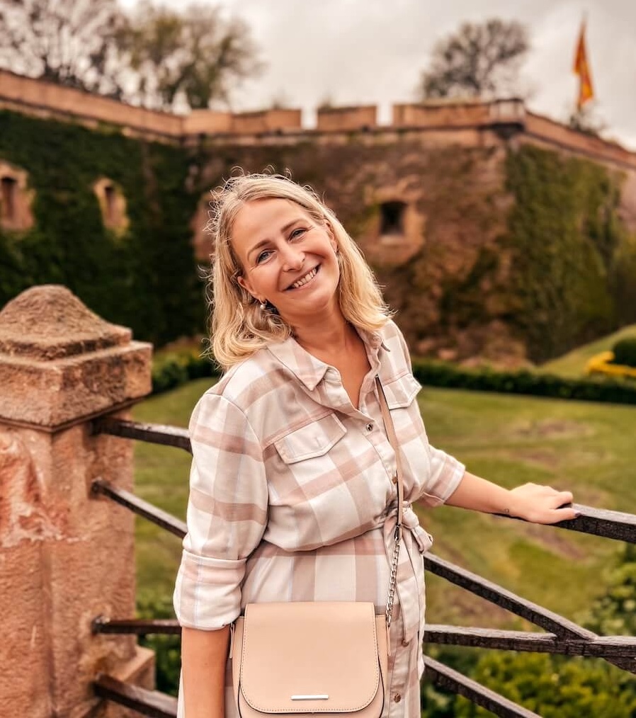 Osobní fotka autorky s úsměvem na mostě u hradu Montjuïc v Barceloně, v pozadí je pevnost a katalánská vlajka. Doklad toho, že Barcelona je skvělá destinace i pro těhotné, pokud hledáte, co navštívit v Barceloně v klidu a s dobrou náladou.