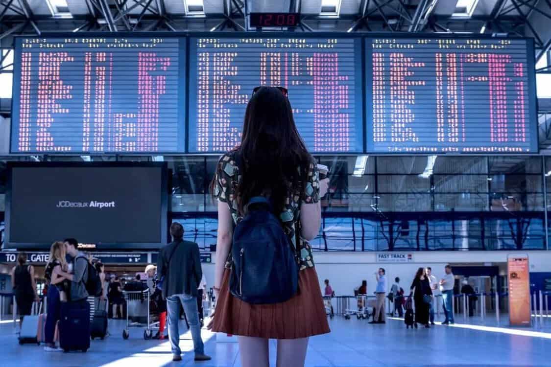Dívka s batohem na letišti, před digitální tabulí. Poprvé na letišti, kam jít, odbavení zavazadel.