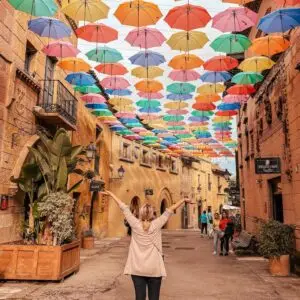 Poble Espanyol, Barcelona. Co videt v Barceloně. Dívka stojící na ulici, nad hlavou barevné deštníky