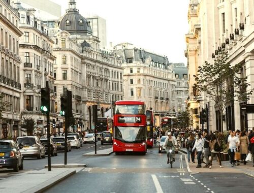 Doprava v Londýně: Pohled na rušnou Regent Street s ikonickým červeným patrovým autobusem (Doubledeckerem), typickými černými taxíky a historickými budovami v pozadí.