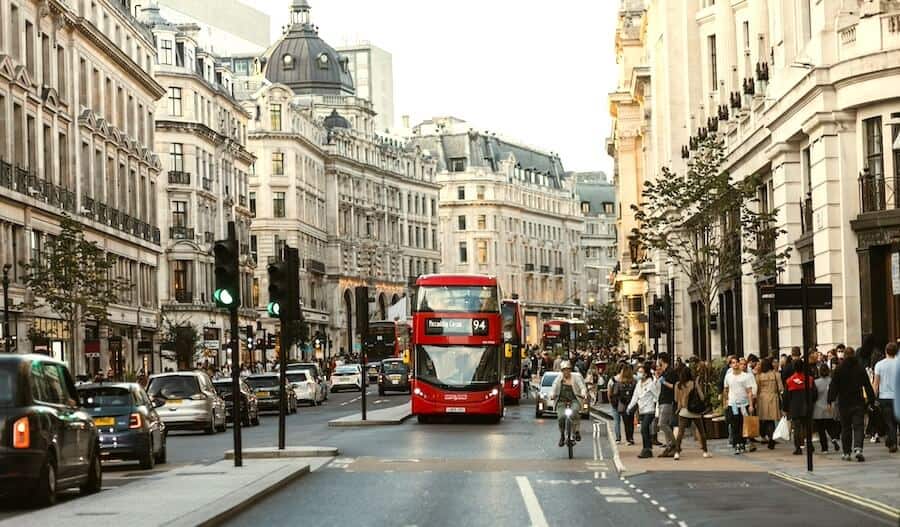 Doprava v Londýně: Pohled na rušnou Regent Street s ikonickým červeným patrovým autobusem (Doubledeckerem), typickými černými taxíky a historickými budovami v pozadí.
