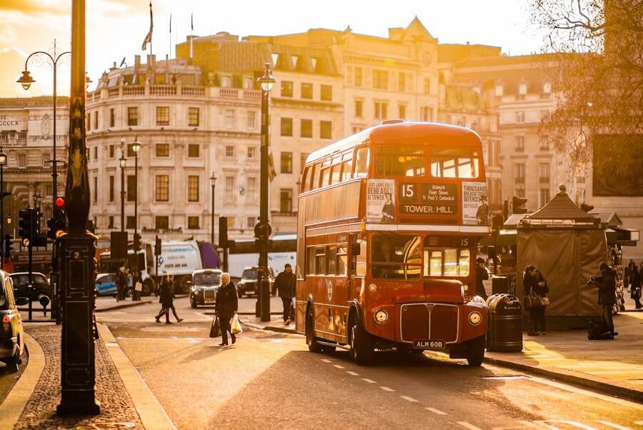 Romantický záběr na historický červený autobus Routemaster na lince 15 směrem na Tower Hill, projíždějící zalitou ulicí v centru. Závěrečný tip pro romantickou dopravu v Londýně při západu slunce.