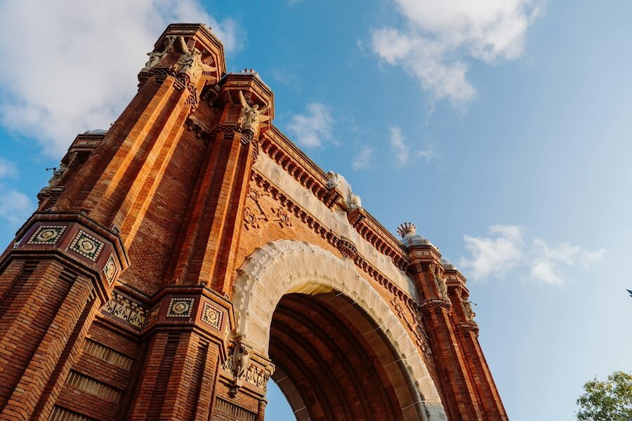 Monumentální Vítězný oblouk (Arc de Triomf) z červených cihel v Barceloně, pohled z podhledu proti modré obloze.
