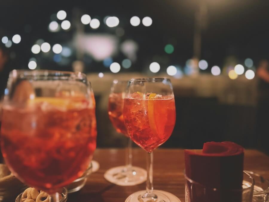 Detailní záběr na sklenice Aperol Spritz na stole v baru, v pozadí rozostřená světla nočního velkoměsta.