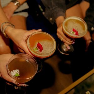 Přátelé si připíjejí barevnými koktejly ozdobenými jedlými květy během večera v baru v centru Barcelony. Noční život v Barceloně.