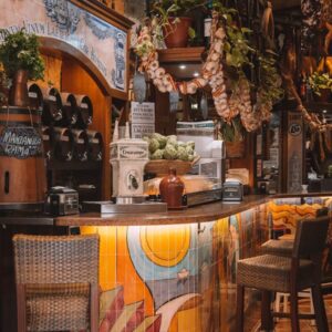 Interiér stylového tapas baru v Barceloně s visícími svazky česneku, keramickými obklady a barovými židličkami.