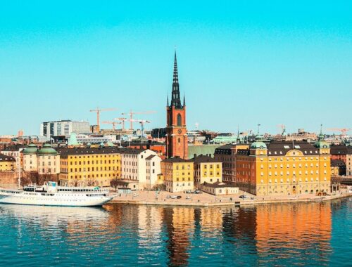 Slunečné panorama Stockholmu z výšky s výhledem na barevné historické budovy, moře a výraznou centralní kostelní věž. Úvodní fotka k článku Stockholm levně.