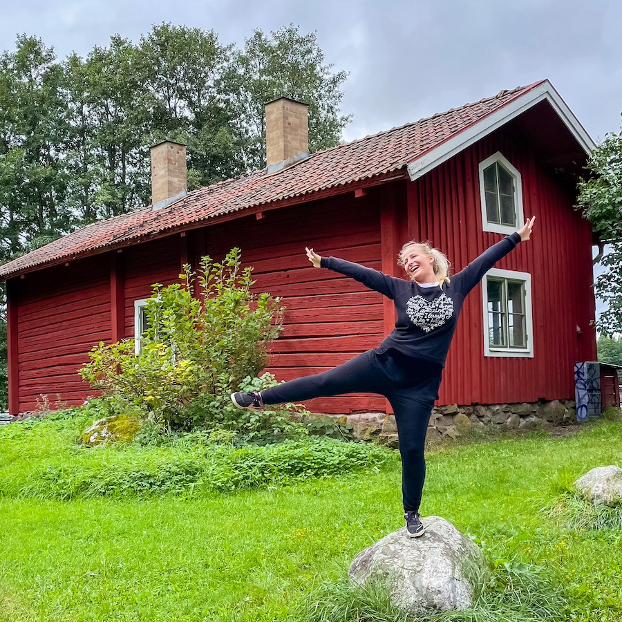 Autorka blogu Blond on the road stojí na kameni a usmívá se, za ní typický červený dřevěný domek. Švédsko, tipy co dělat zdarma ve Stockholmu.