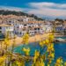 Tradiční bílé domečky v Calella de Palafrugell s výhledem na moře a rozkvetlé žluté keře.