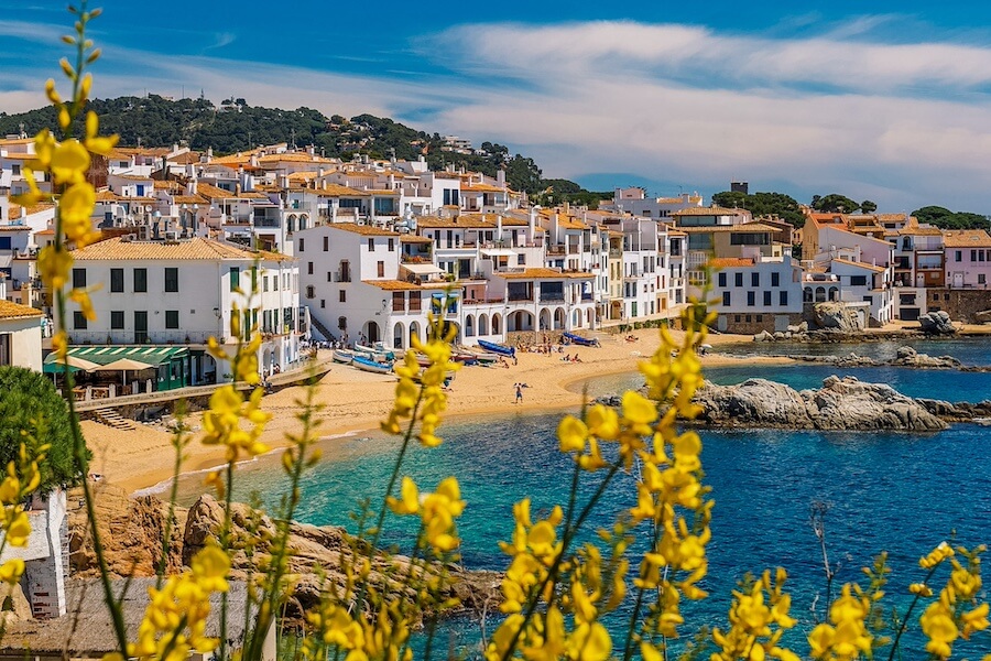 Tradiční bílé domečky v Calella de Palafrugell s výhledem na moře a rozkvetlé žluté keře.
