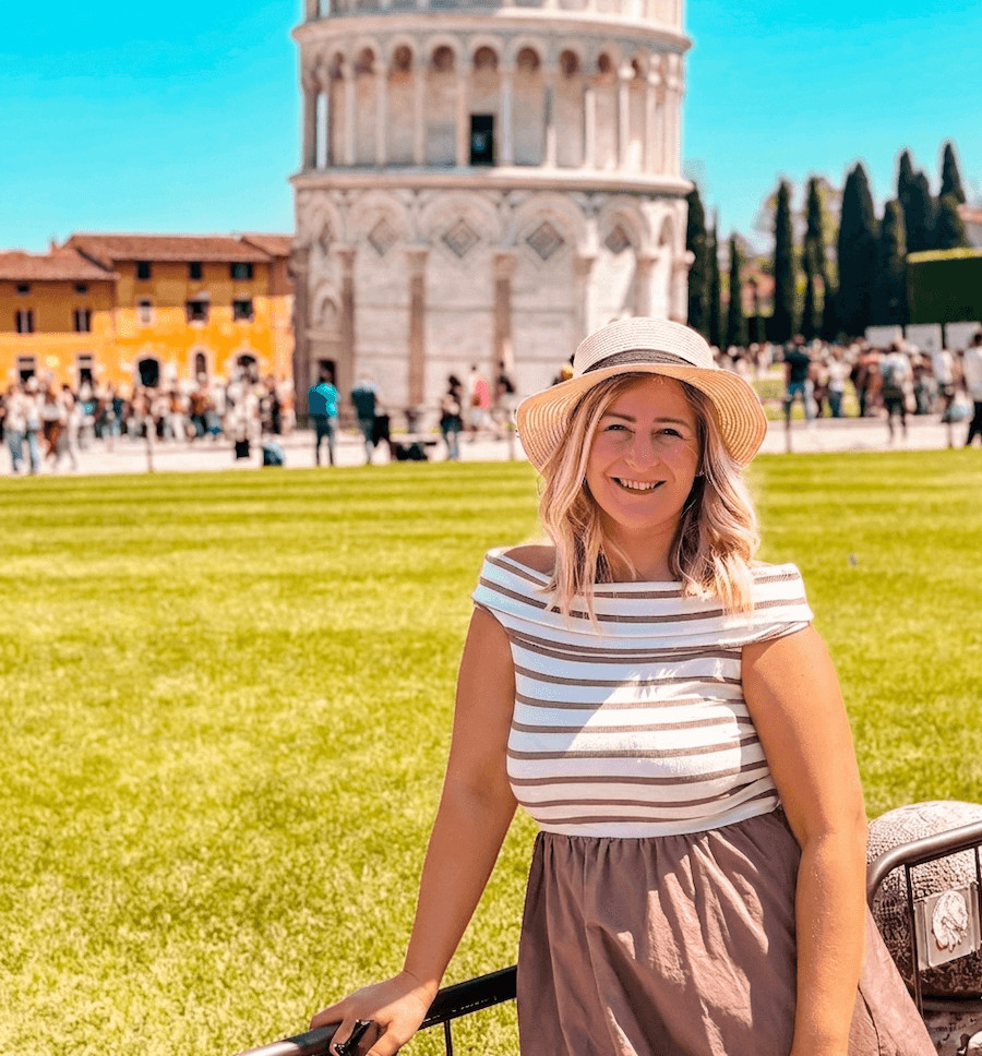 Blogerka s kloboukem na travnaté ploše Piazza dei Miracoli, v pozadí Šikmá věž v Pise, článek Pisa za jeden den.