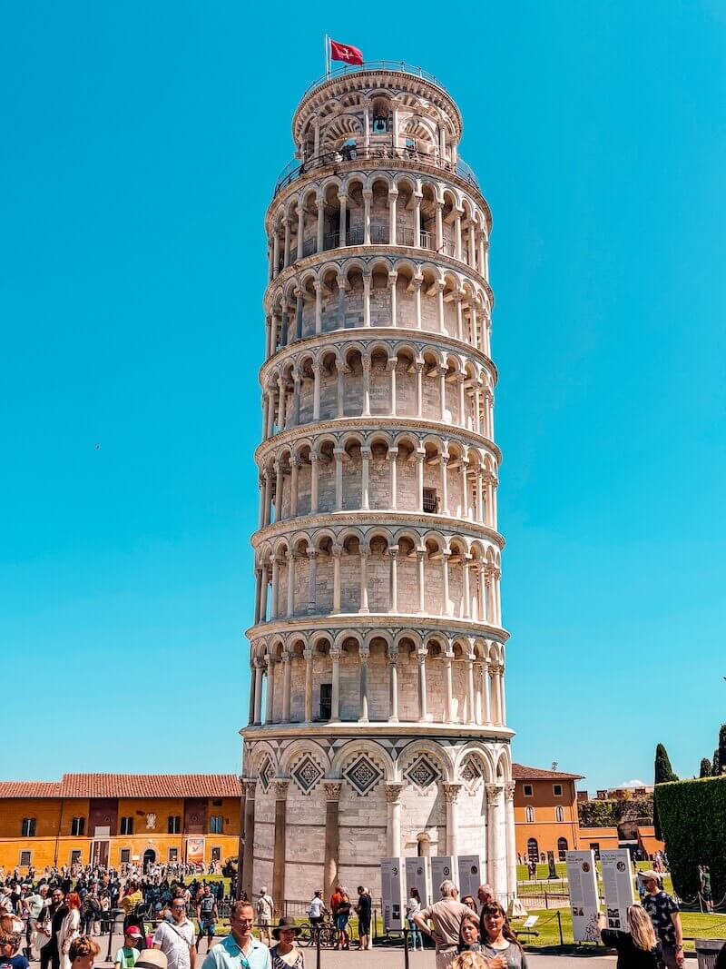 Detailní pohled na slavnou Šikmou věž v Pise s italskou vlajkou na vrcholu, článek Pisa za jeden den.