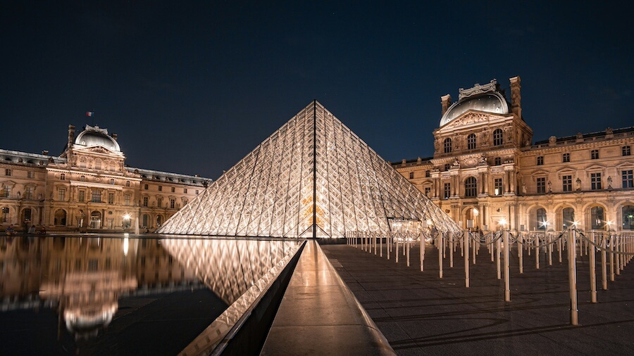 Osvětlená budova muzea Louvre a skleněná pyramida za noci - jedno z nejslavnějších míst Paříže