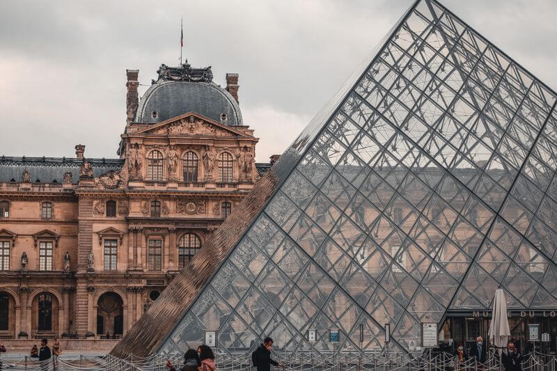 Ikonický záběr na skleněnou pyramidu Louvre v Paříži, v pozadí historická budova muzea