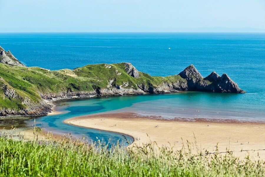 Pohled na pláž Three Cliffs Bay s tyrkysovým mořem a skalnatými výběžky. Místa ve Walesu, která vypadají jako Nový Zéland