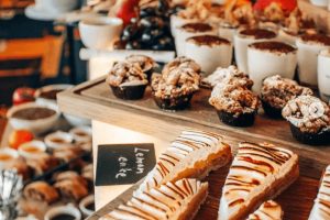 Tip na nejlepší brunch v Praze - Mama Shelter Prague. Detail na citronové řezy s pusinkou na dřevěném podnosu, v pozadí bohatý sladký bar. Tip na sladké gastro zážitky v Praze.