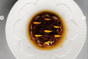 Zážitková gastronomie v restauraci Reason v Praze: Detail na minimalistický fine dining dezert na bílém talíři se zlatým hnízdem a kapičkami. Tip na nejlepší luxusní restaurace v článku kam na jídlo v Praze.