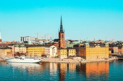 Slunečné panorama Stockholmu z výšky s výhledem na barevné historické budovy, moře a výraznou centralní kostelní věž. Úvodní fotka k článku Stockholm levně.