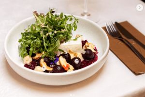 Esteticky laděná miska se salátem z červené řepy, doplněným čerstvými bylinkami, oříšky a kousky fety nebo tofu. Příklad originálního ukrajinského rostlinného pokrmu, který najdete v Praze, když nevíte, kam na jídlo. Podnik SLOVO na Vinohradech.