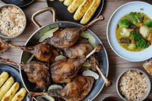 Tradiční česká kuchyně talíře na stole, hlavní talíř opečená husa, na dalších talířích knedlíky. Pohled shora. Fotografie z restaurace Výčep Korunní v Praze.