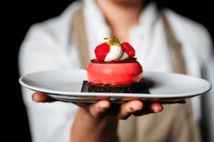 Nejlepší cukrárny v Praze: Detail na moderní růžový dezert s čerstvými malinami a krémem, podávaný na bílém talíři. Cukrář Skála je tip na sladkou tečku při hledání, kam na jídlo v Praze.