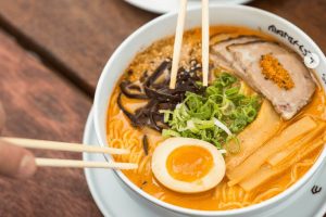 Autentický ramen v Praze: Hůlky nabírají nudle z misky s vývarem, vepřovým masem, vejcem a bambusem. Průvodce asijskou kuchyní při hledání nejlepší restaurace v Praze - Manifesto Market.