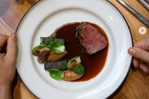 Perfektní hovězí steak v Praze v restauraci Mazel: Záběr z ptačí perspektivy na talíř s medailonkem masa, omáčkou demi-glace a pečenou zeleninou (kapustičky). Gastro zážitek v článku kam na jídlo v Praze.