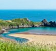 Pohled na pláž Three Cliffs Bay s tyrkysovým mořem a skalnatými výběžky. Místa ve Walesu, která vypadají jako Nový Zéland